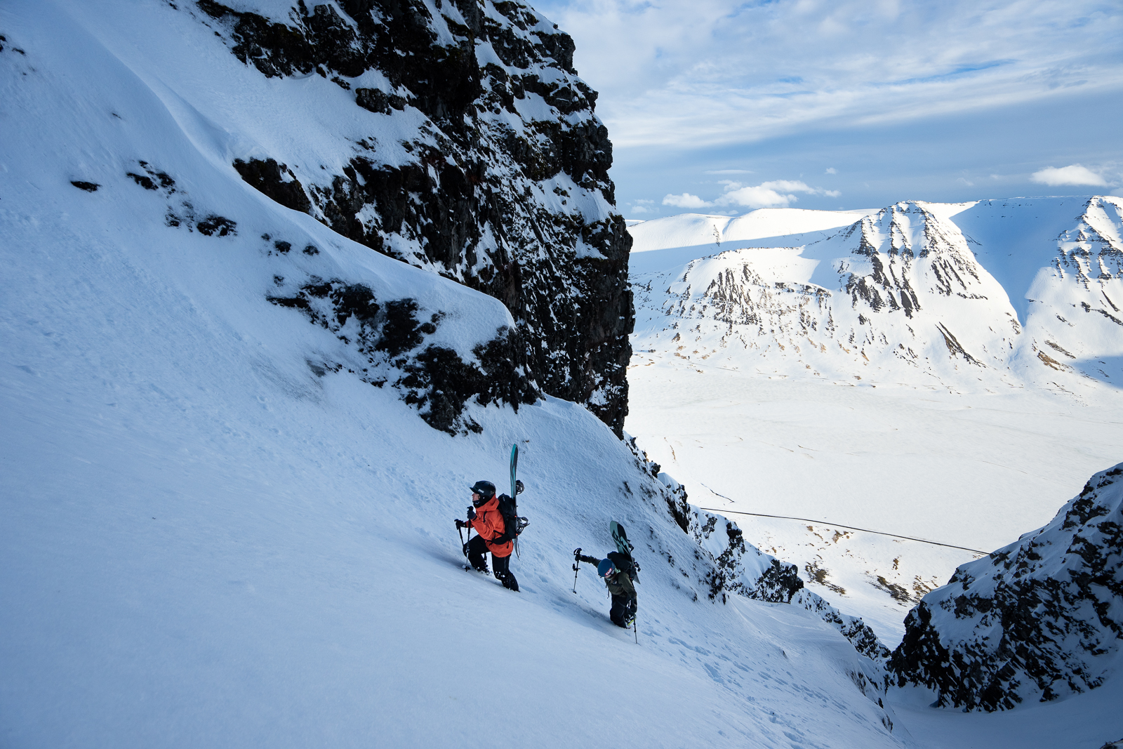 Robin Van Gyn and Elena Hight climb a couloir in Iceland's Westfjords with snowboards on their backs. 